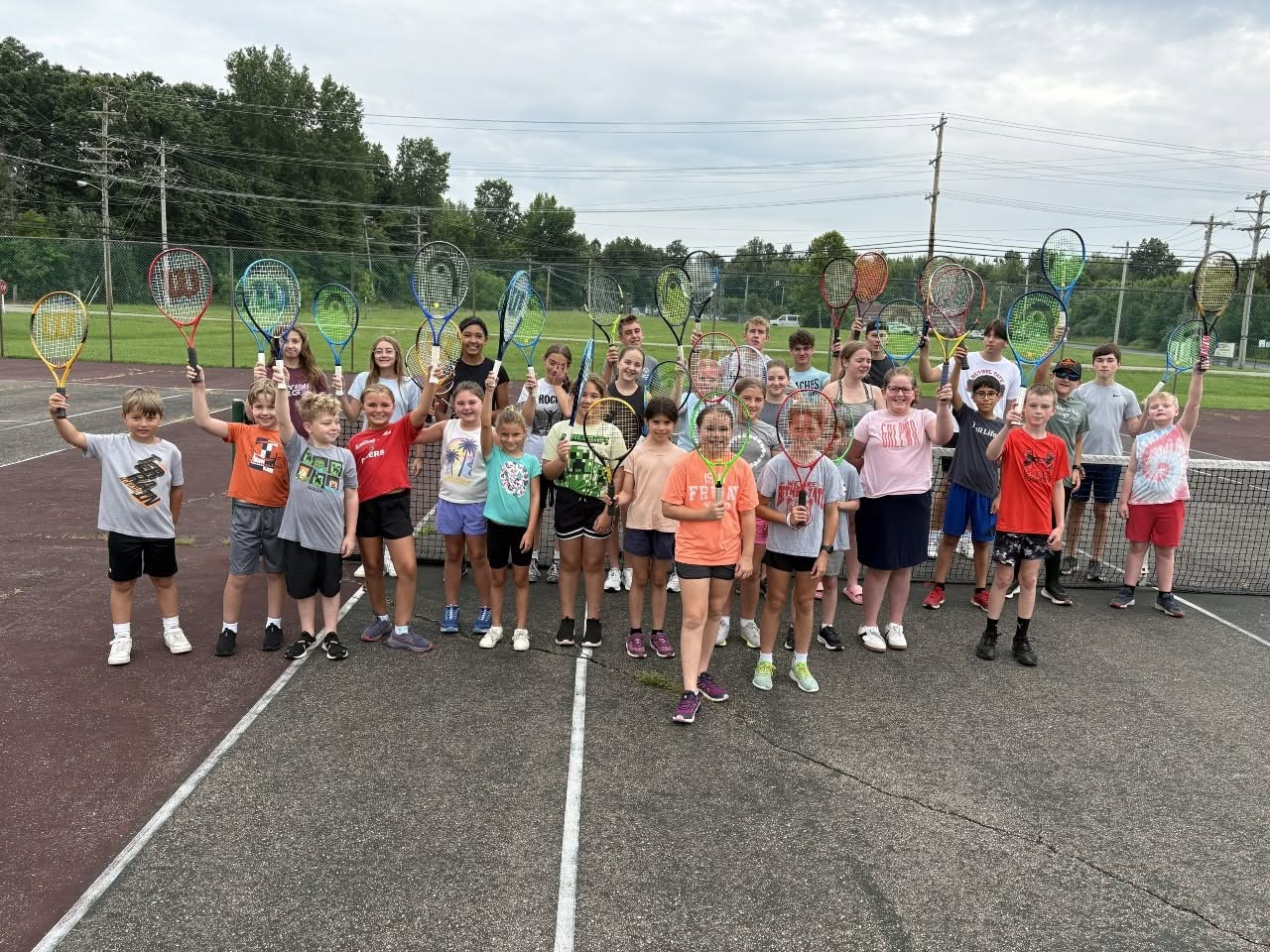 Kids hold up rackets at a Bethel-Tate youth tennis clinic